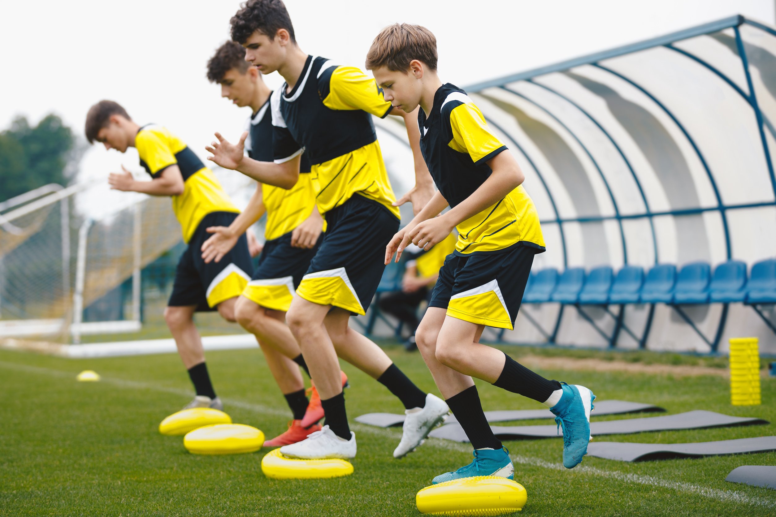 Sports Balance Training. Teenage Football Players Standing On Balance Cushions During Football Training Unit. Youth Football Club Players at Summer Practice Camp